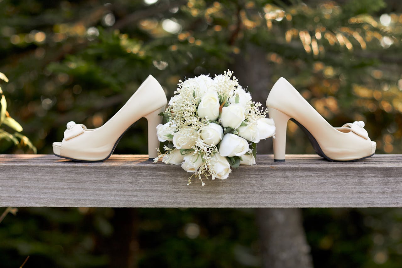 Beautiful wedding shoes and white bouquet on a rustic wooden beam outdoors.